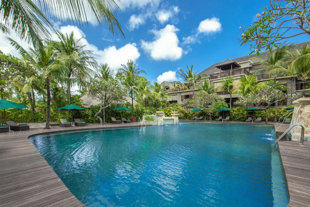 Resort swimming pool with palm trees and loungers under blue sky