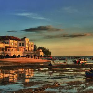 Coastal mosque lit by sunset with boats resting on shore at low tide