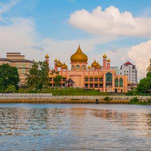 Golden-domed mosque beside river with urban buildings and trees