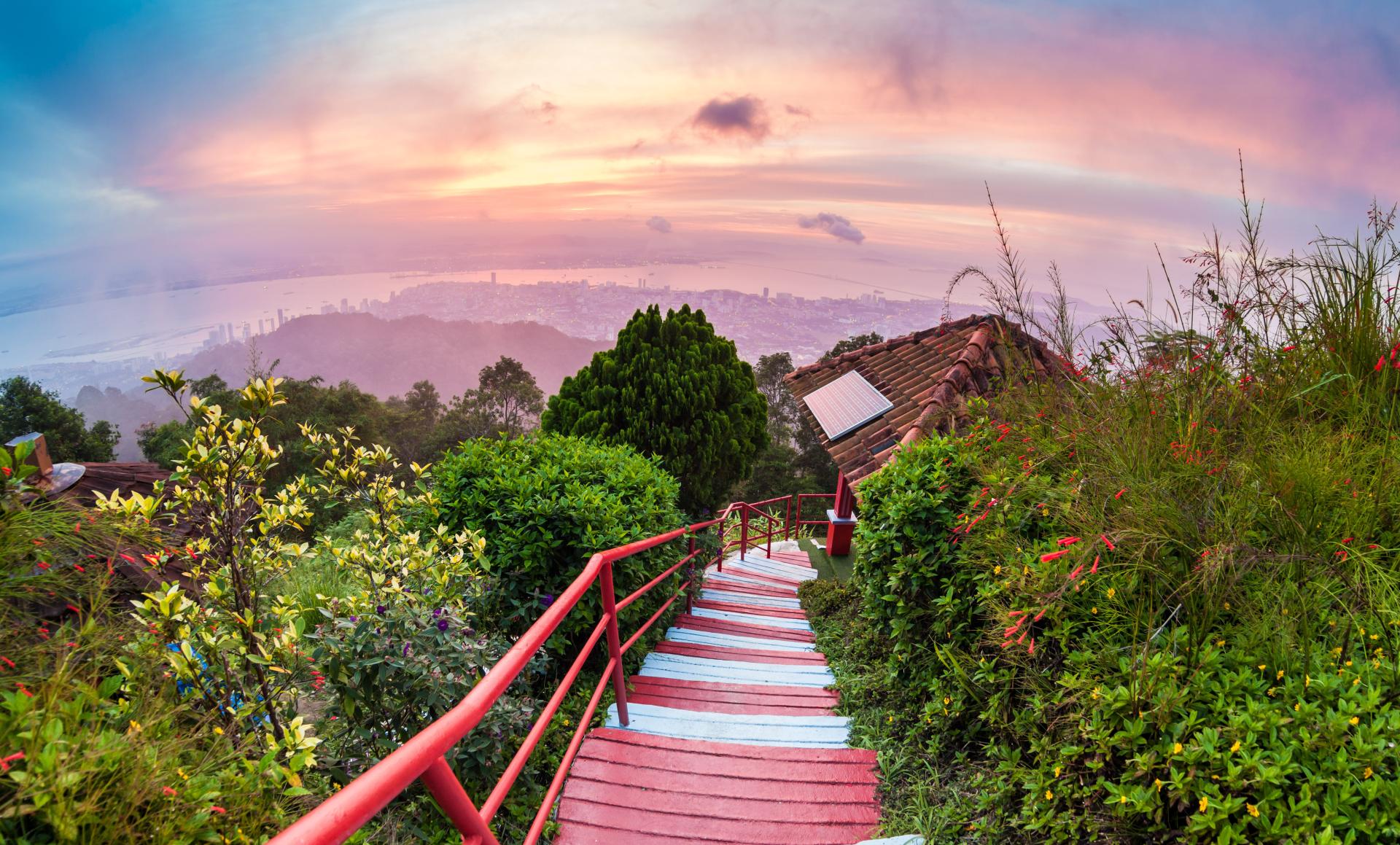 Red and white stairway descending hillside with cityscape at sunset