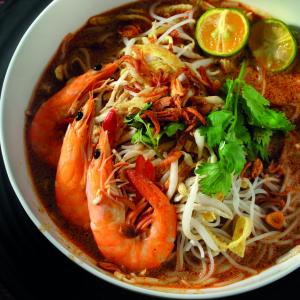Bowl of spicy prawn noodle soup with lime, herbs, and noodles
