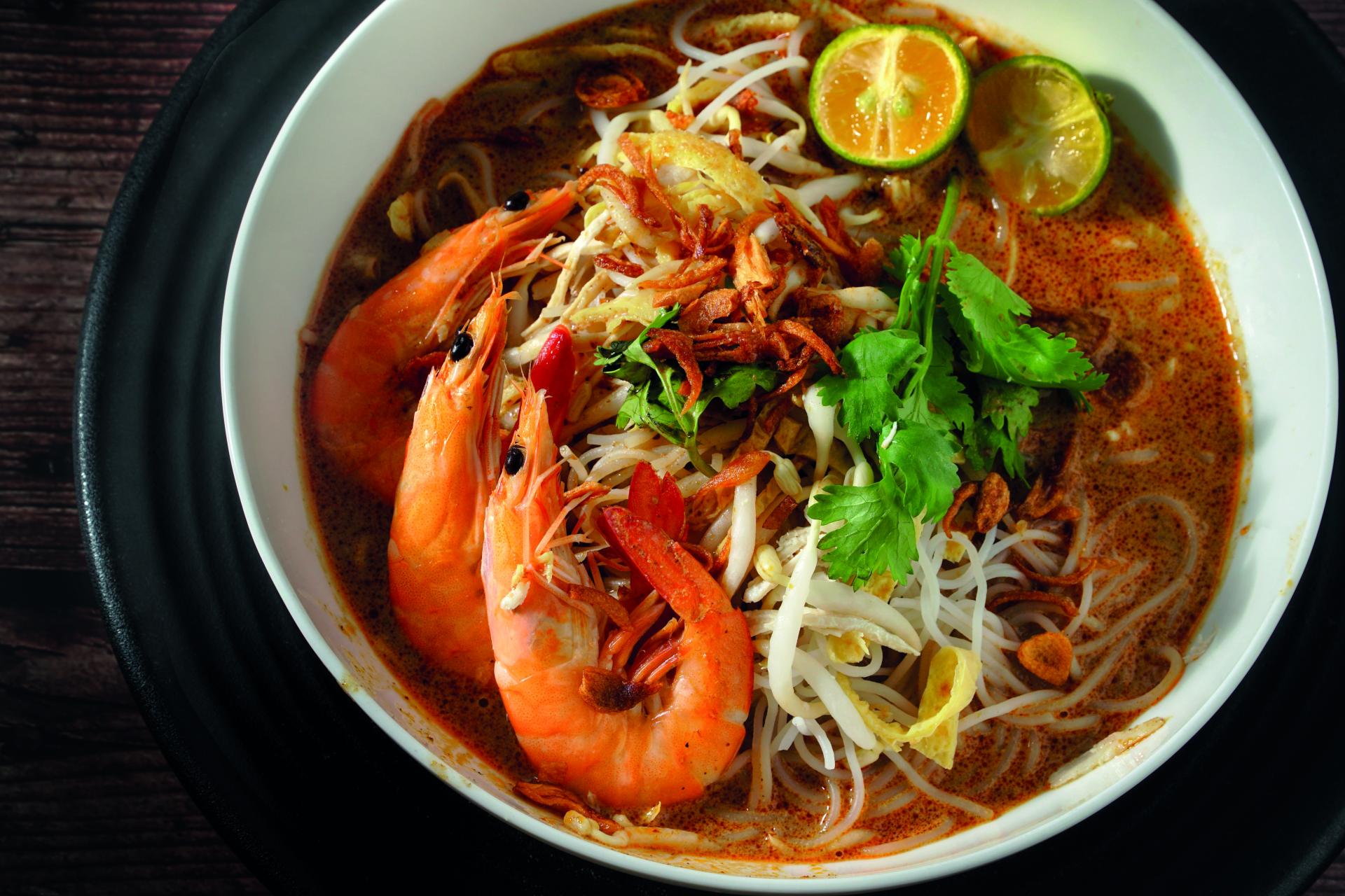 Bowl of spicy prawn noodle soup with lime, herbs, and noodles
