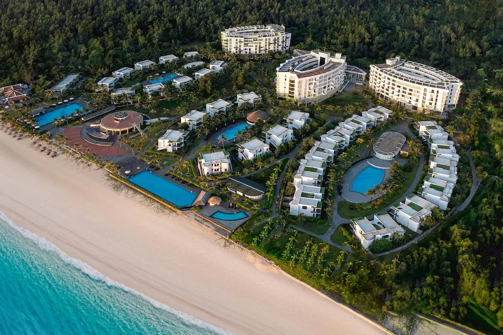 Aerial view of luxury beachfront resort with pools and villas along sandy beach