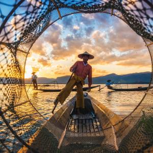Fishermen at sunset using traditional nets and leg-rowing on boats with mountains in background
