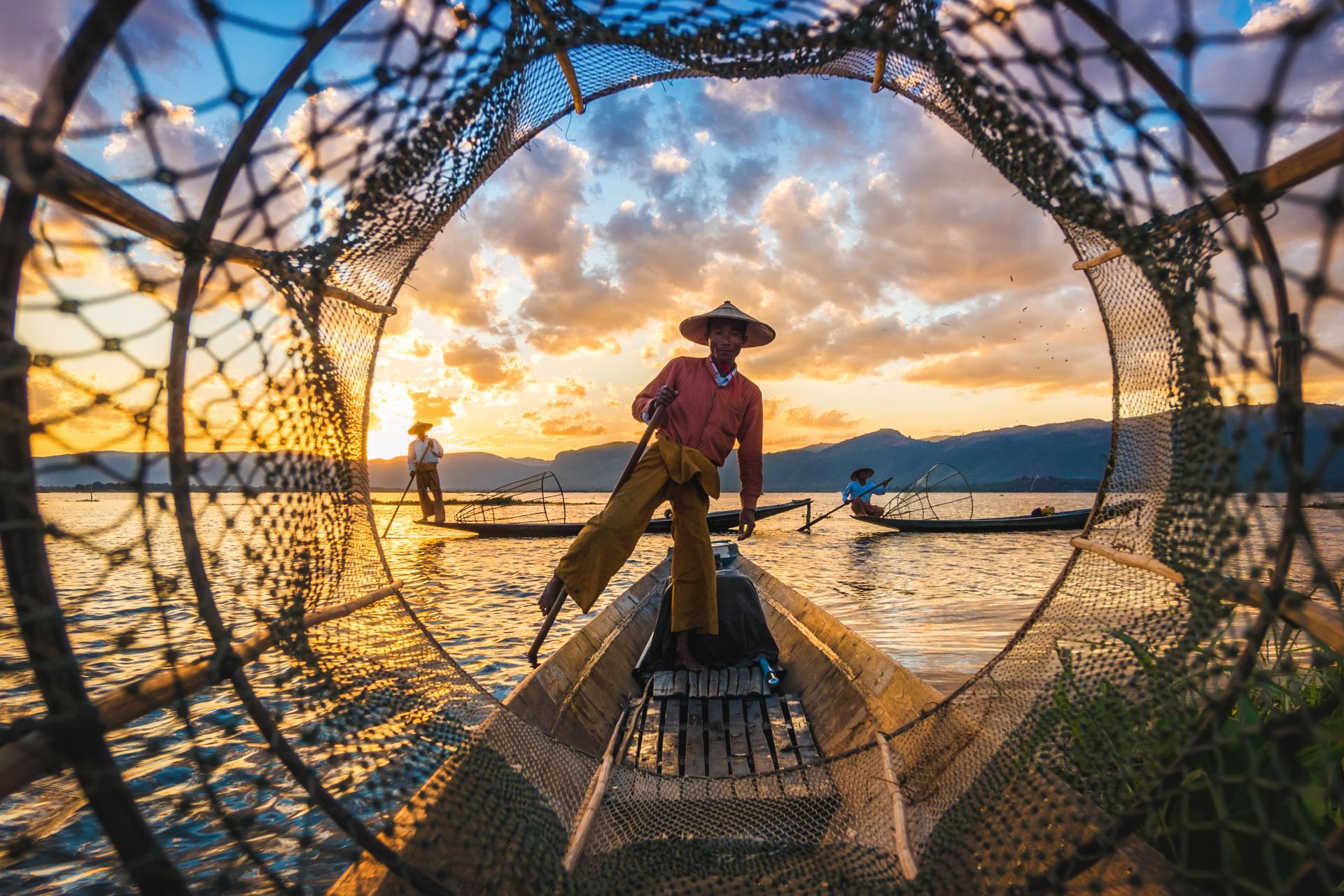 Fishermen at sunset using traditional nets and leg-rowing on boats with mountains in background