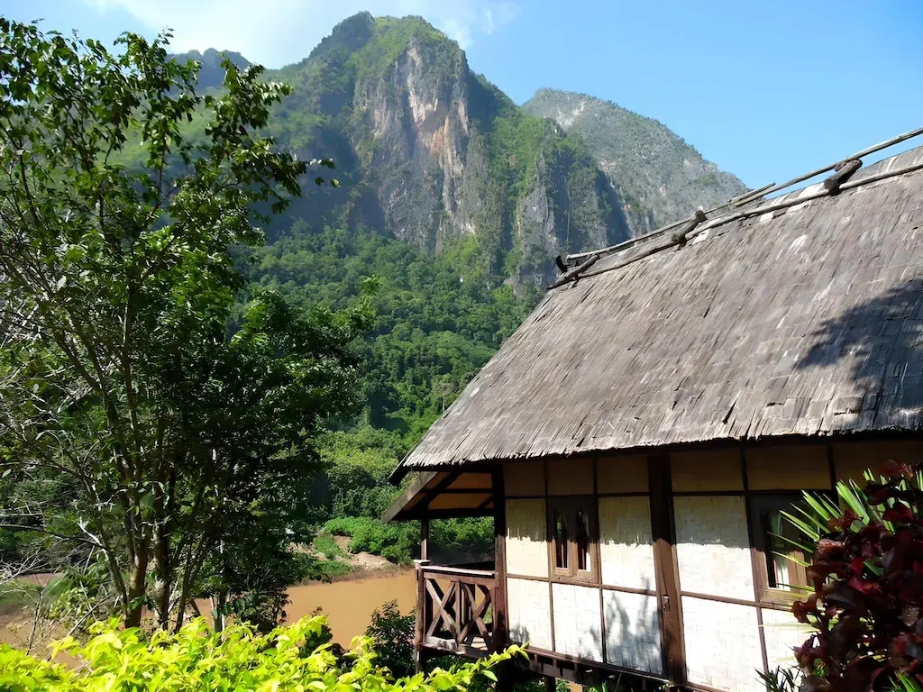 Thatched riverside cottage next to river with mountain backdrop