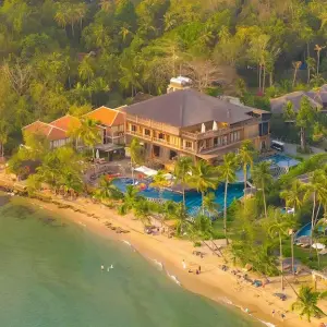Aerial view of a beachfront tropical resort with pools, palm trees, and sandy beach
