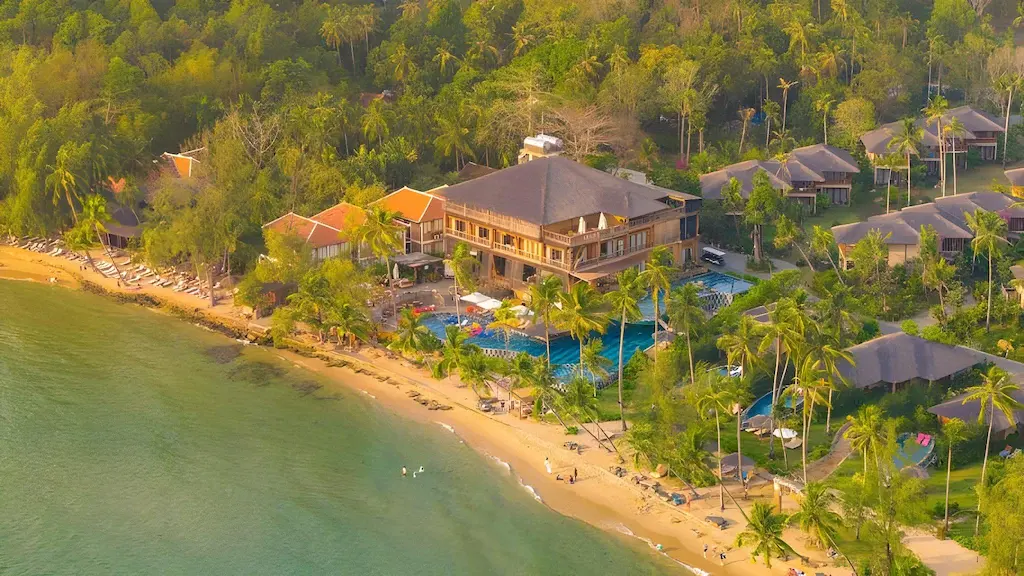 Aerial view of a beachfront tropical resort with pools, palm trees, and sandy beach