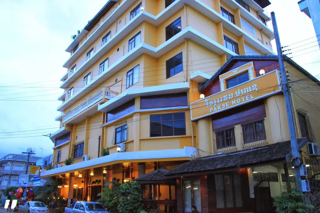 Yellow multi-story Pakse Hotel building with parked cars at dusk