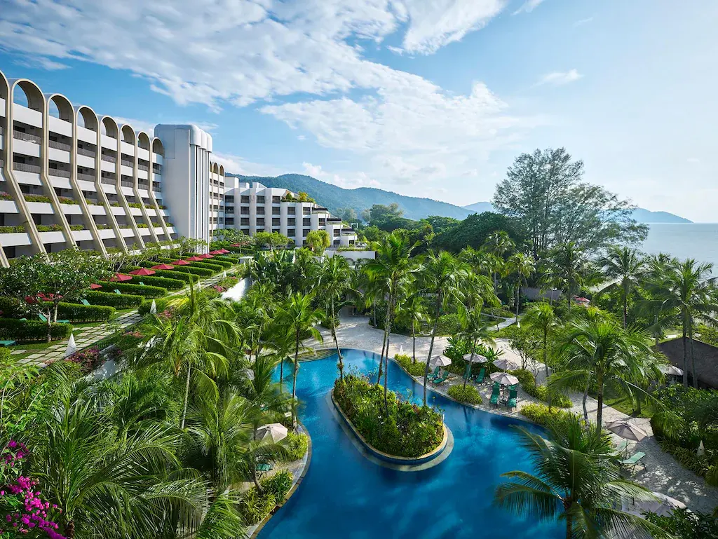 Pool area surrounded by palm trees and garden at Parkroyal Penang Resort under blue sky