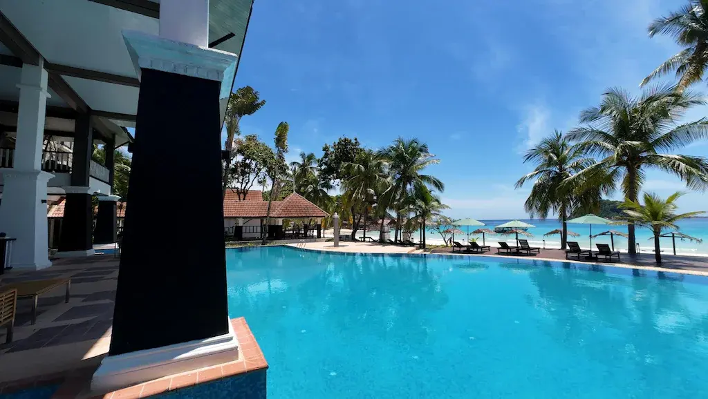Poolside view of swimming pool with palm trees and beach umbrellas by the ocean
