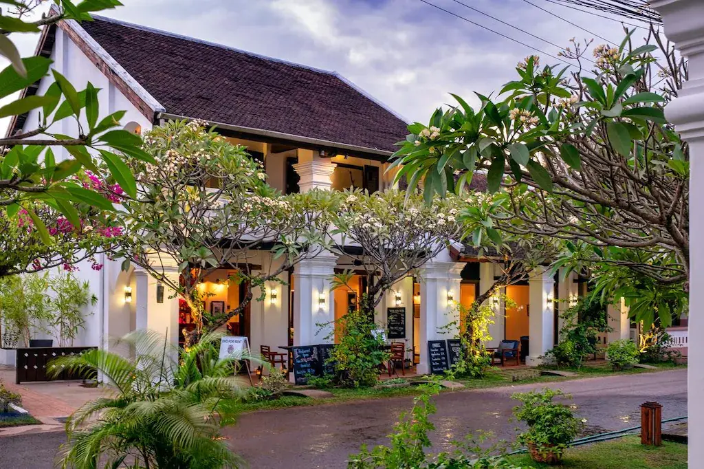 White two-story building with dark roof and garden trees at dusk