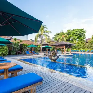 Hotel outdoor pool with blue loungers, green umbrellas, fountain, and palm trees