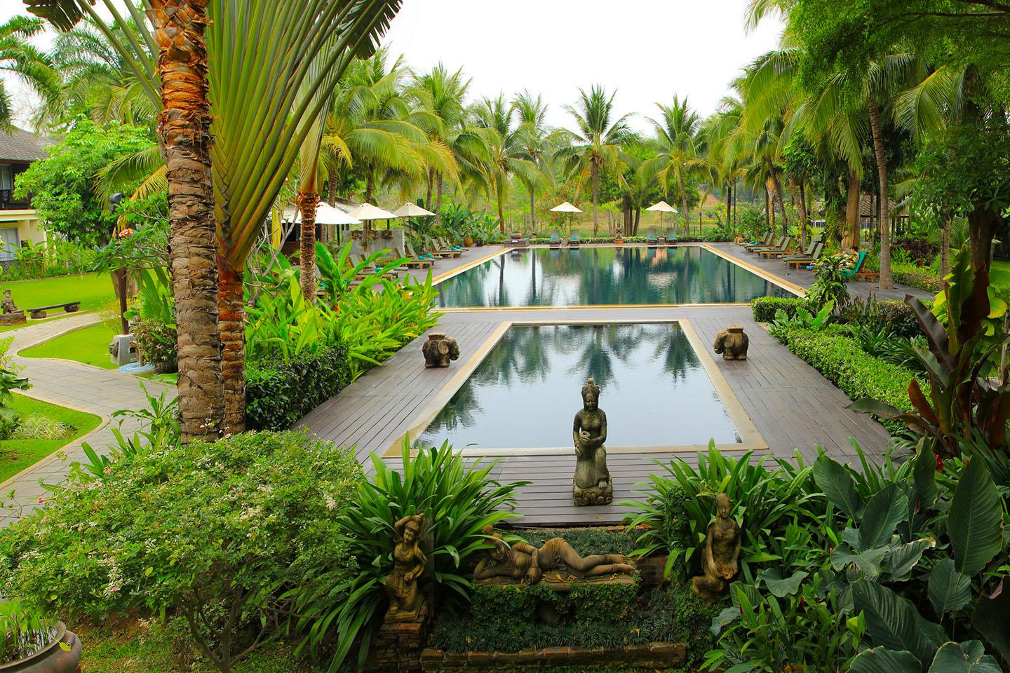Swimming pool surrounded by palm trees and statues in a tropical resort garden