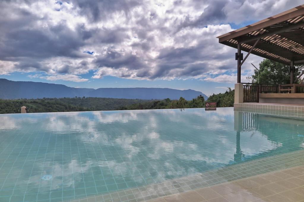Infinity pool with mountain view and pergola under cloudy sky
