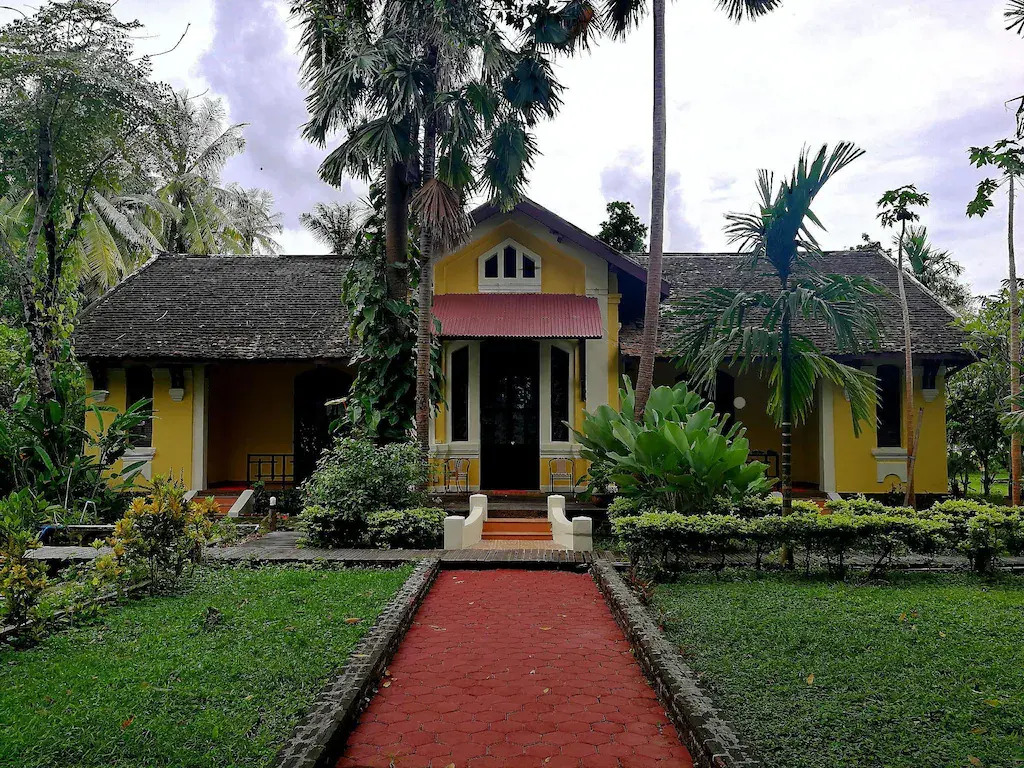Yellow building of Sala Done Khone Hotel surrounded by tropical trees and garden
