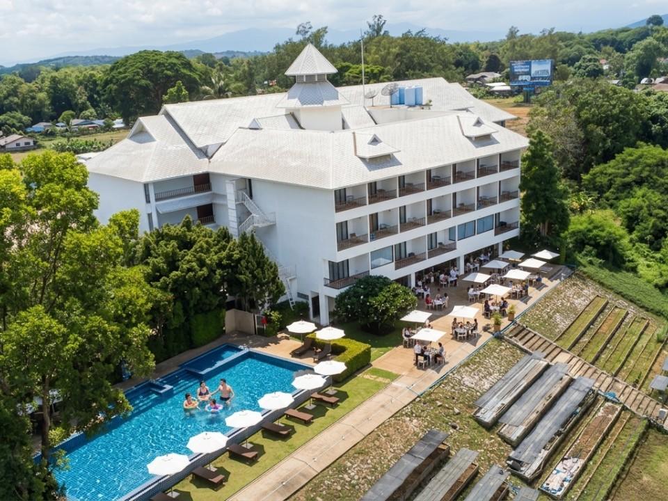 Four-story hotel with outdoor pool and terrace dining area surrounded by greenery