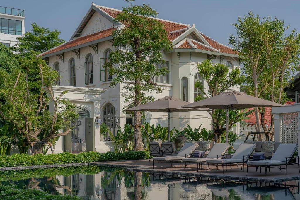 Colonial-style villa with pool and lounge chairs surrounded by trees at Souphattra Heritage Vientiane