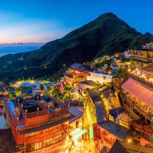 Mountain village lit with warm lights at dusk overlooking ocean and hills