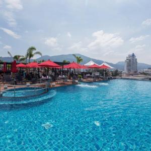 Rooftop infinity pool with red umbrellas, loungers, and mountain views under a blue sky.