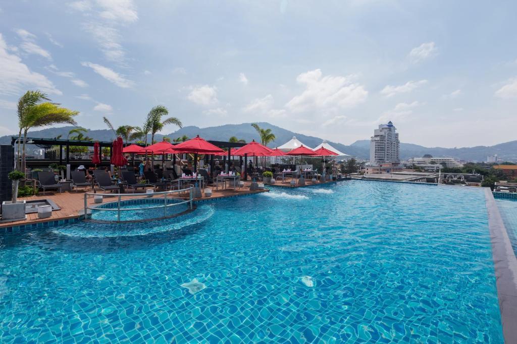 Rooftop infinity pool with red umbrellas, loungers, and mountain views under a blue sky.