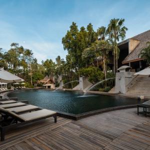 Resort pool with sun loungers, umbrellas, water fountains, palm trees, and wooden deck