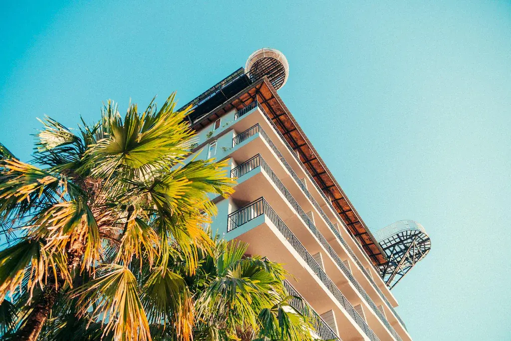 Low angle view of The Elephant Crossing Hotel building with palm trees and clear blue sky.