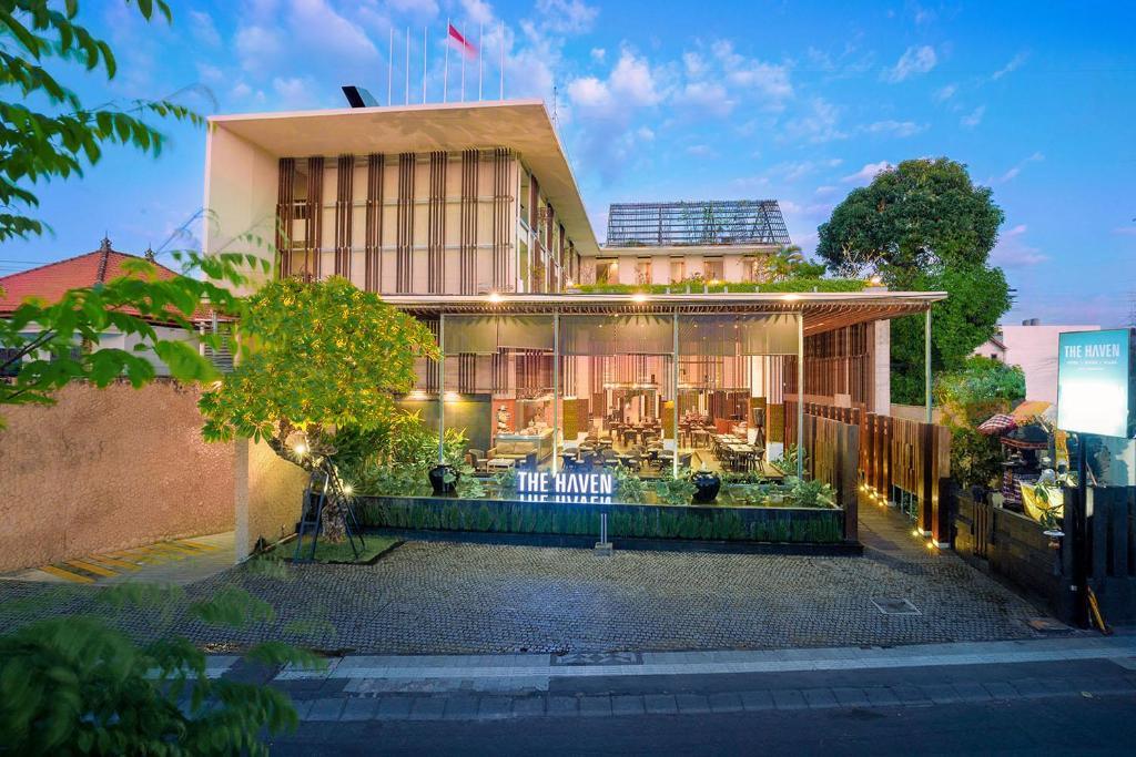 Exterior of modern hotel with open-air glass dining area and illuminated sign at dusk