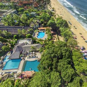 Aerial view of beachfront resort with swimming pools, palm trees, and colorful beach umbrellas by ocean