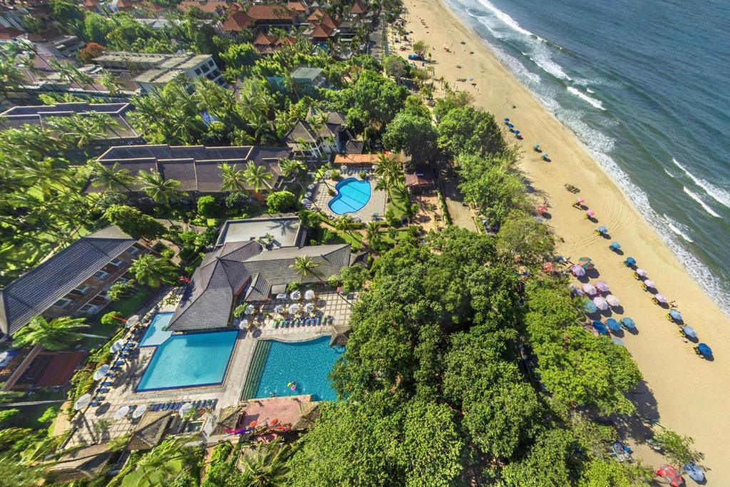 Aerial view of beachfront resort with swimming pools, palm trees, and colorful beach umbrellas by ocean