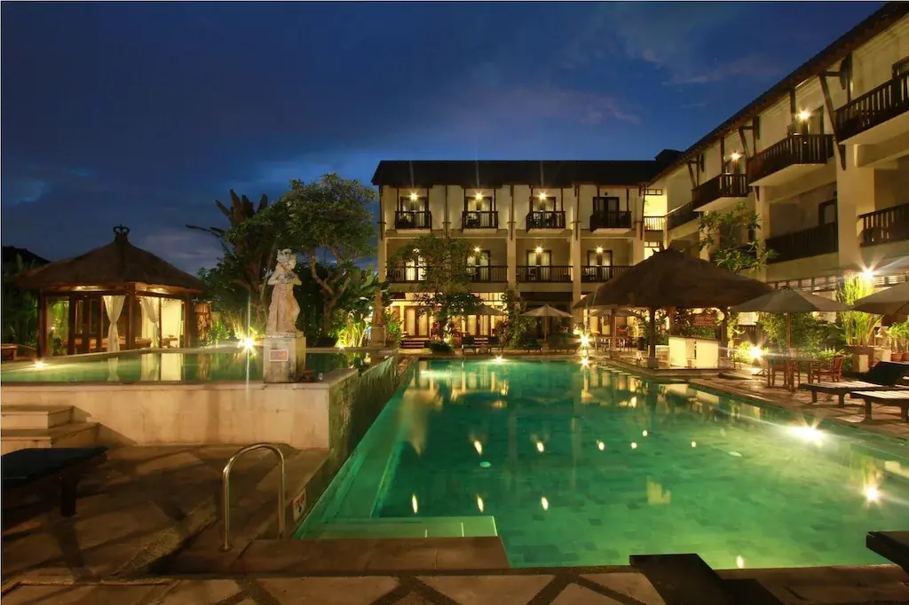 Lit swimming pool and resort balconies at night with tropical decor