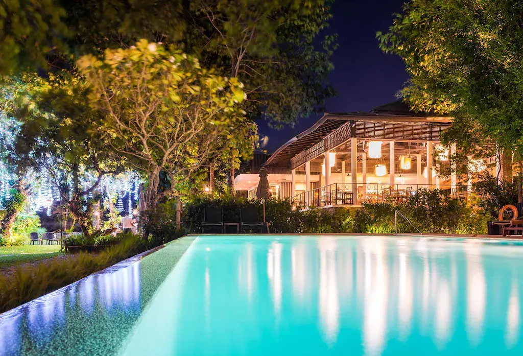 Night view of The River Resort with glowing pool and illuminated dining area surrounded by trees