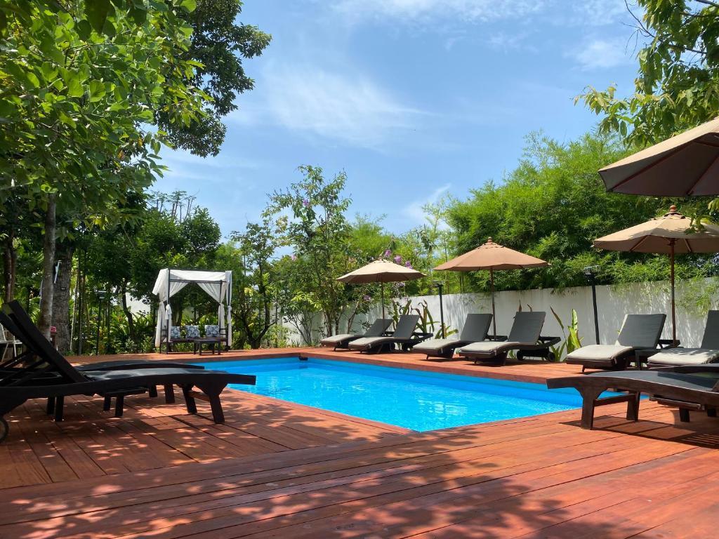Outdoor pool with sun loungers and umbrellas surrounded by lush green trees at The Riviera Champasak.