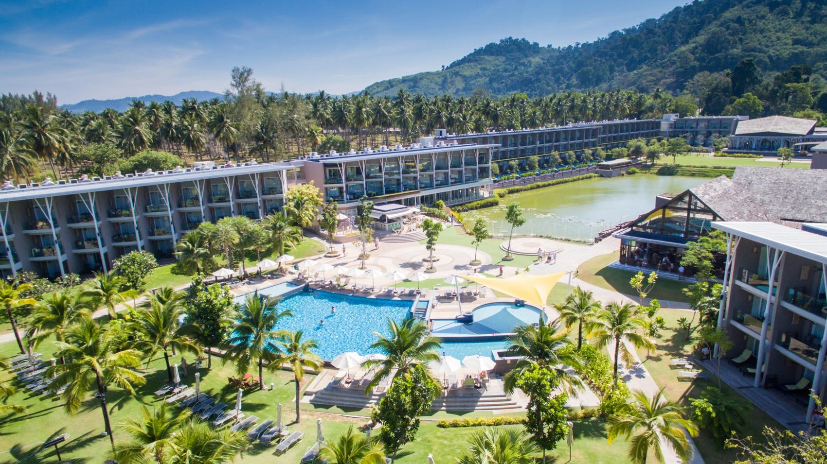 A resort with swimming pool, palm trees, and green hills in the background