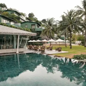 Luxury resort with infinity pool, green buildings, palm trees, and outdoor seating area