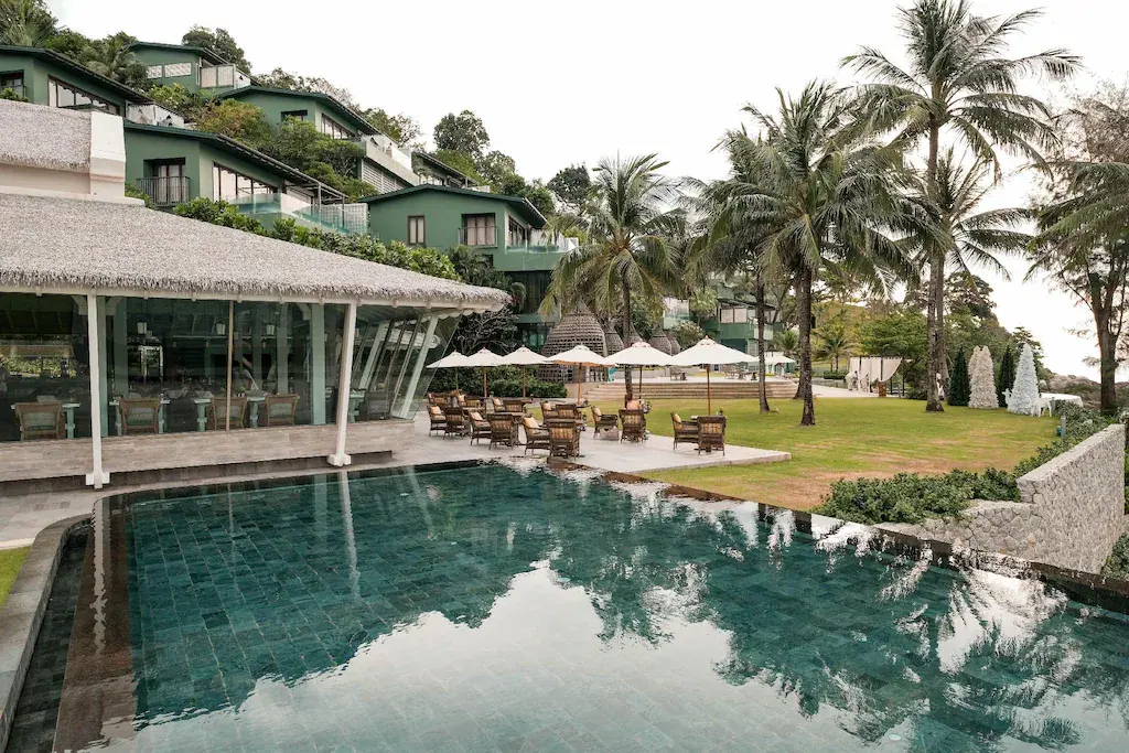 Luxury resort with infinity pool, green buildings, palm trees, and outdoor seating area