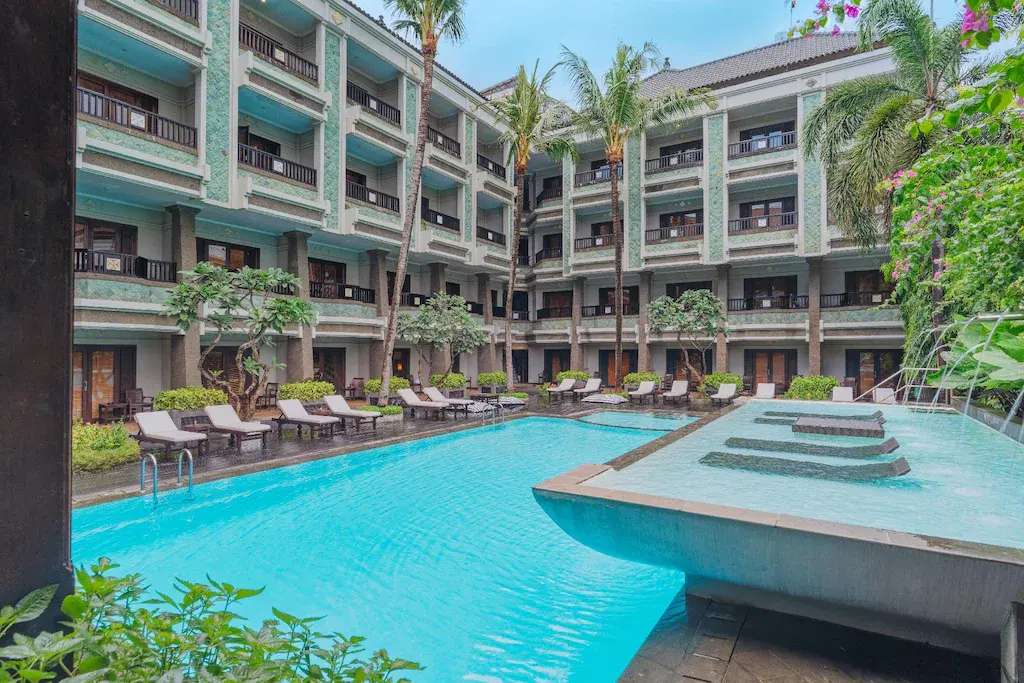 Outdoor swimming pool with lounge chairs and palm trees at The Vira Bali resort courtyard