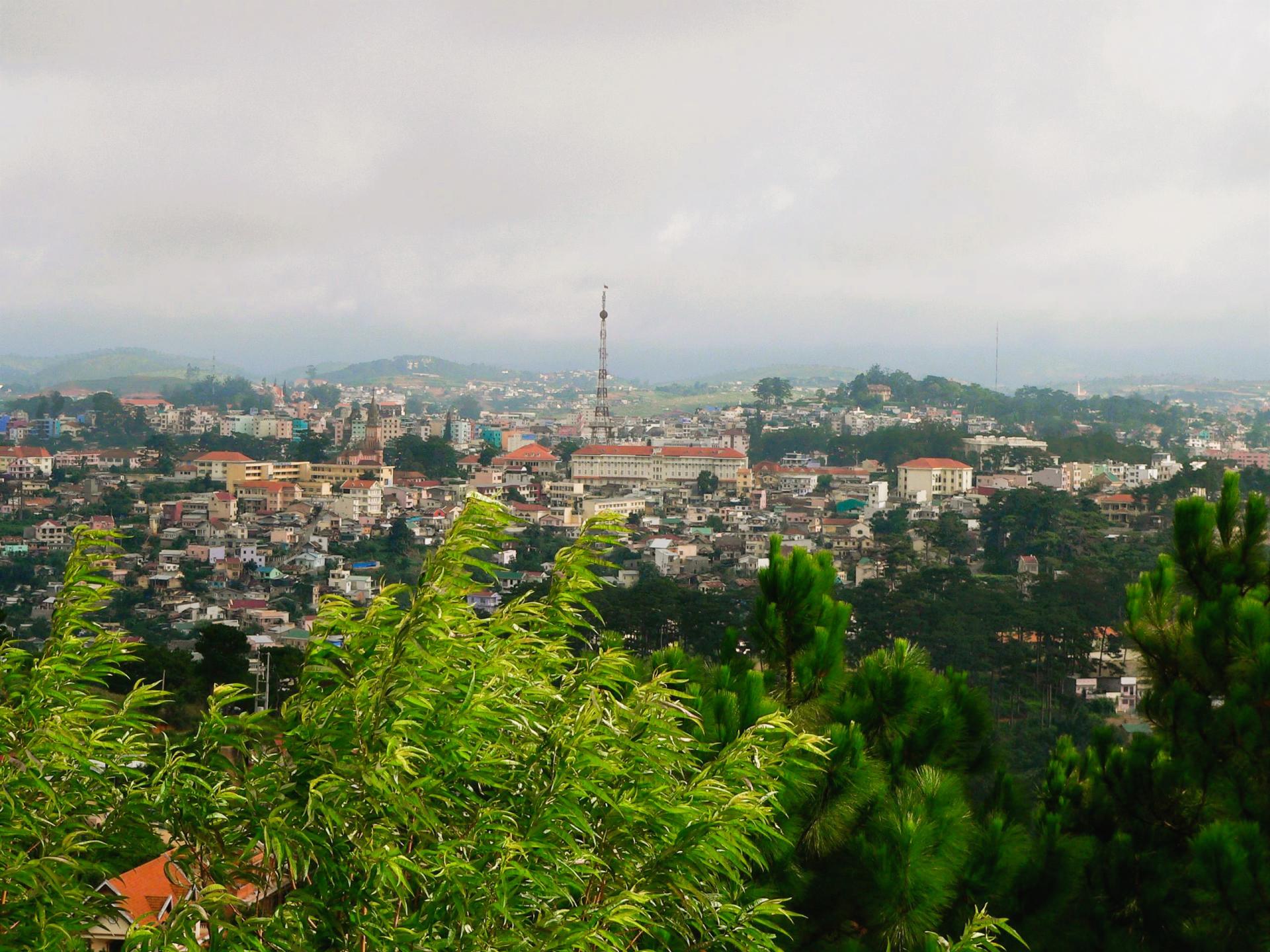 Dalat cityscape with buildings and green trees under a cloudy sky,