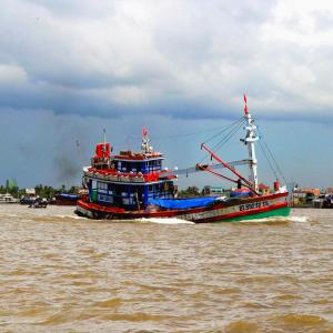Colorful traditional wooden boat moving on muddy river near buildings under cloudy sky