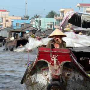 Woman wearing conical hat on traditional wooden boat on river near riverside village