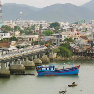 Blue fishing boat near bridge over calm water and city with hills