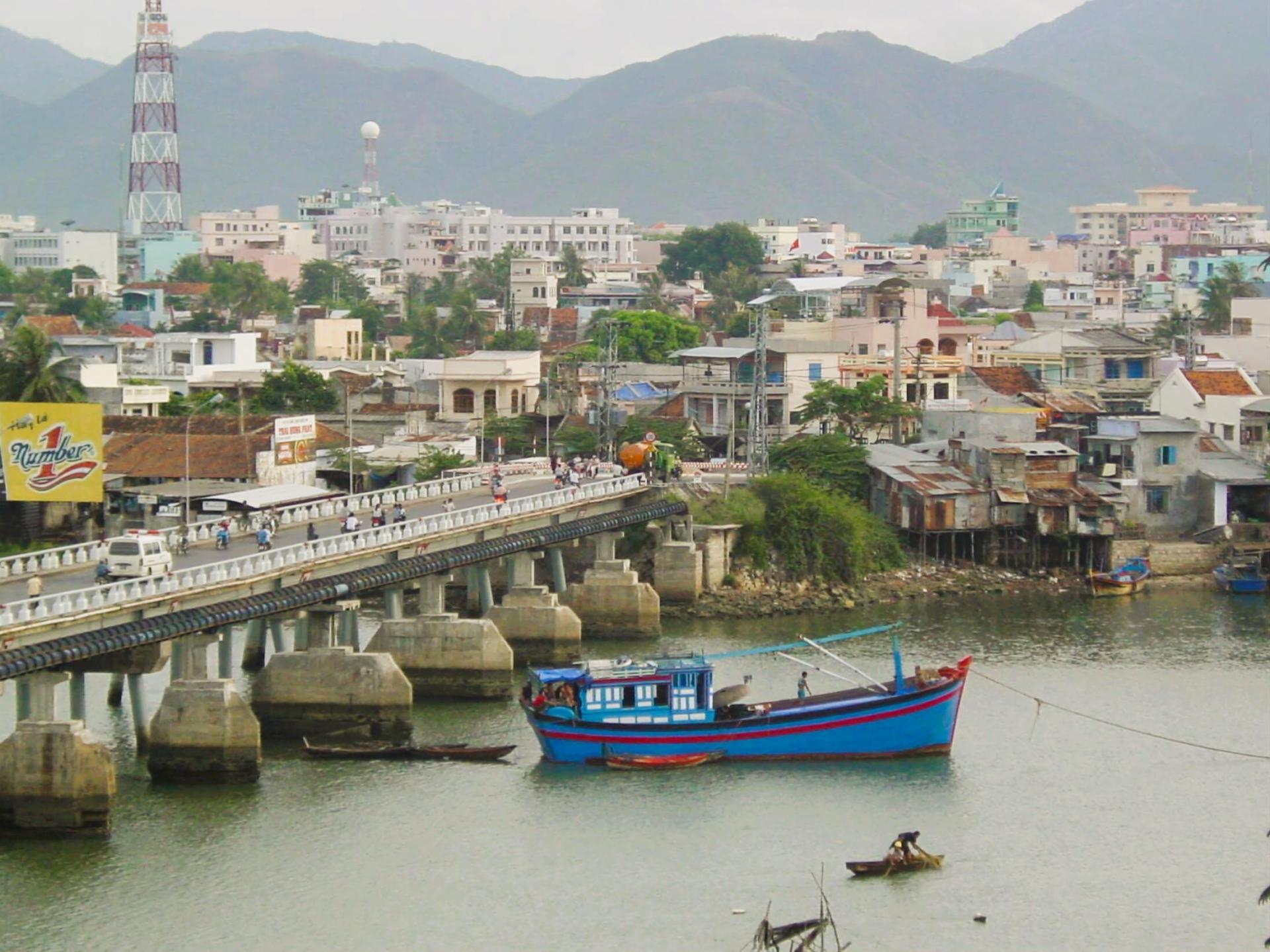 Blue fishing boat near bridge over calm water and city with hills