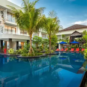 Hotel courtyard with pool, palm trees, red loungers and blue umbrellas