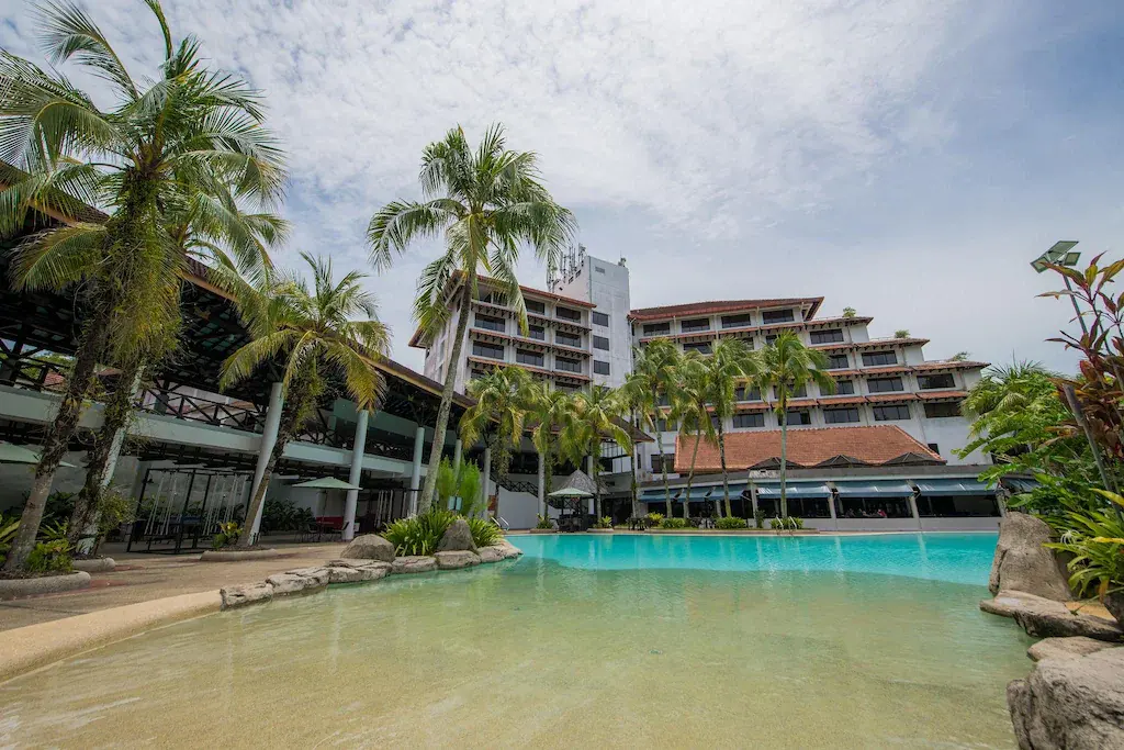 Resort hotel building with large swimming pool and palm trees on a partly cloudy day