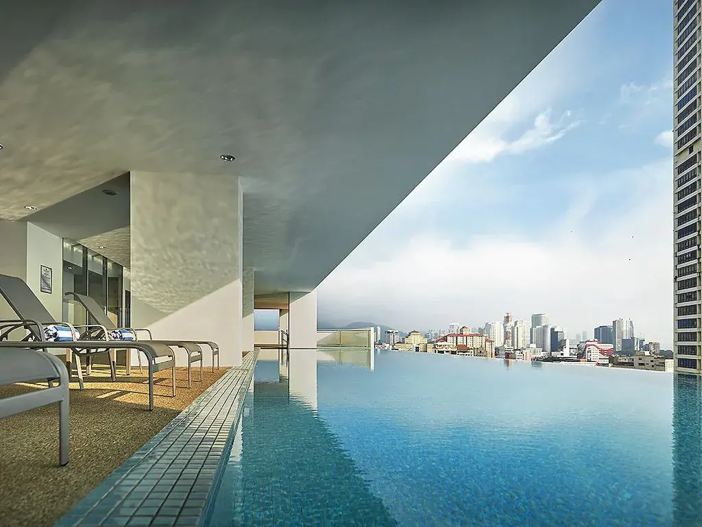 Rooftop infinity pool and loungers overlooking city skyline under partly cloudy sky