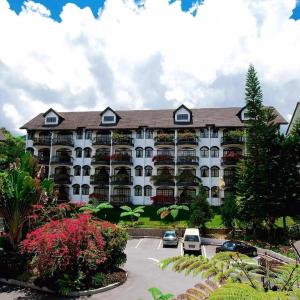 White hotel building with balconies, garden, parked cars, and cloudy sky