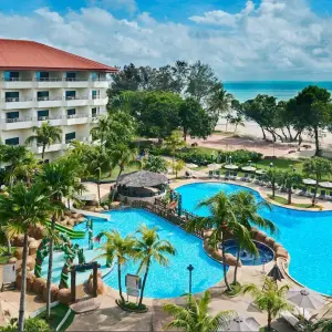 Beachfront resort with large swimming pool, palm trees, and ocean view