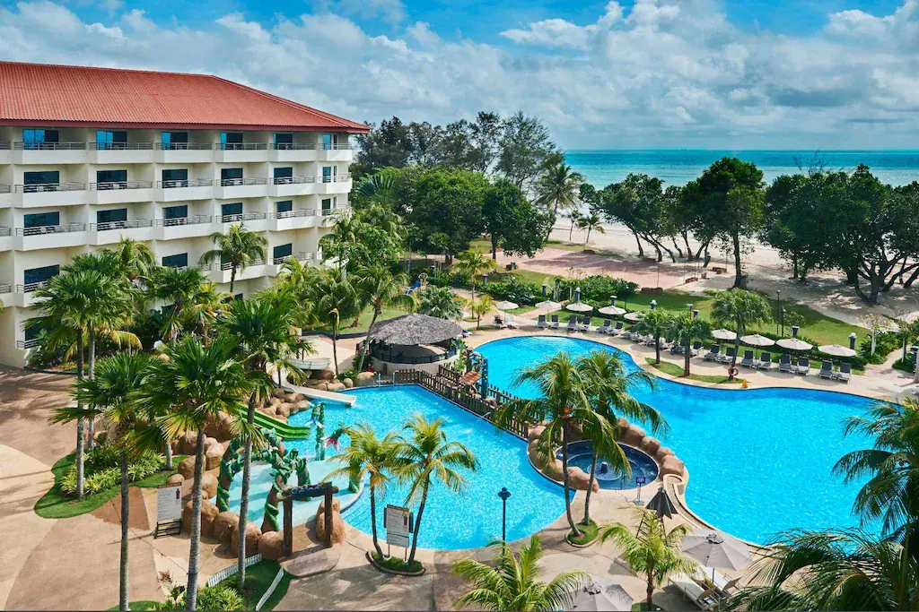 Beachfront resort with large swimming pool, palm trees, and ocean view