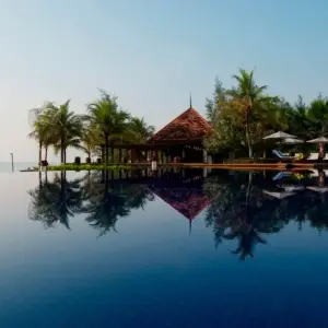 Infinity pool reflecting palm trees and tropical resort pavilion