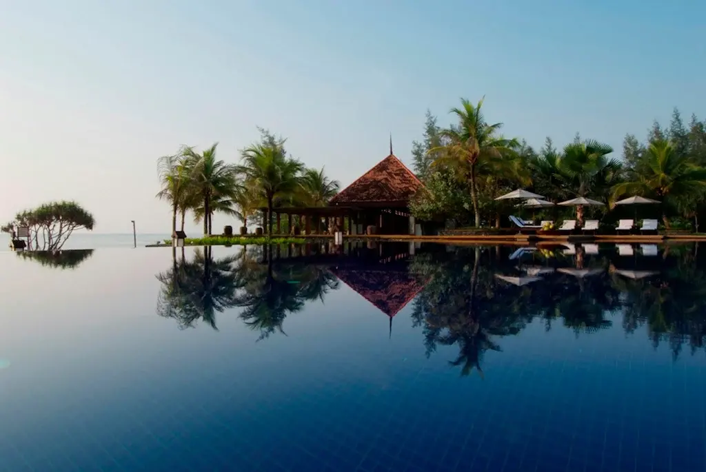 Infinity pool reflecting palm trees and tropical resort pavilion